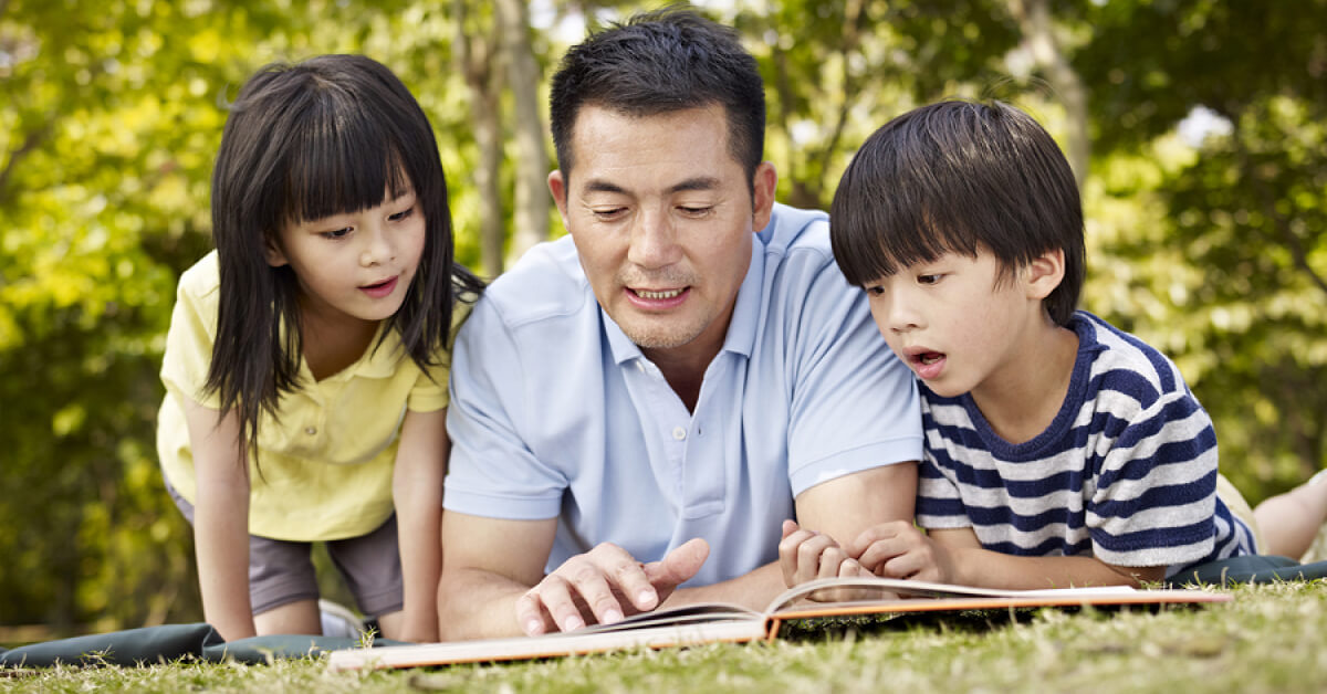 Seorang bapak membaca buku bersama kedua anaknya agar anak dapat berkembang secara optimal